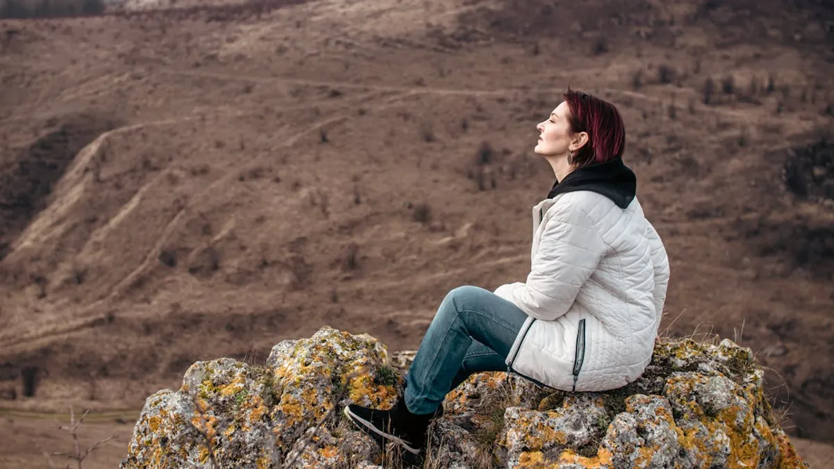 Woman enjoying solitude on a rocky mountain peak, eyes closed in leisure.