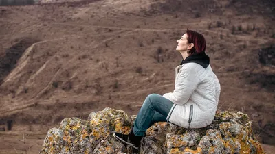 Woman enjoying solitude on a rocky mountain peak, eyes closed in leisure.
