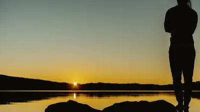 Silhouette of a person watching a serene sunrise by a lake in Cape Town, South Africa.
