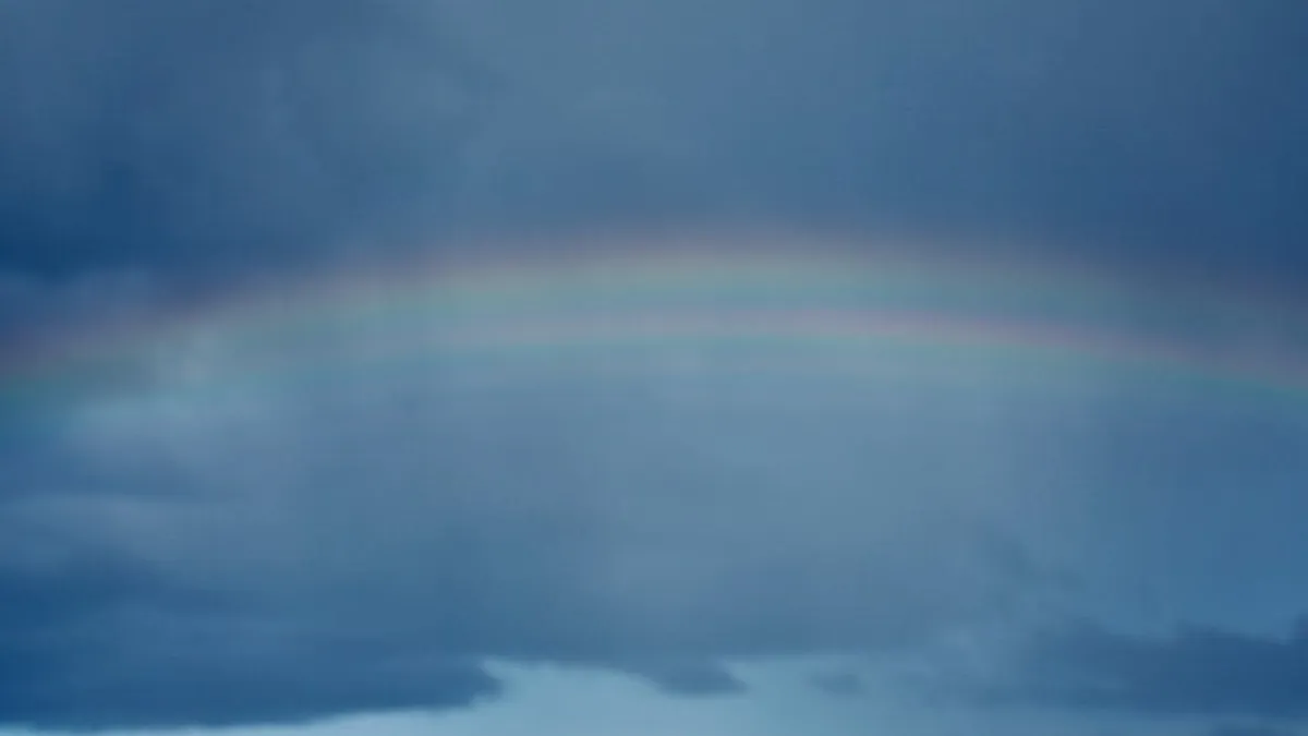 A tranquil scene of a rainbow arching across a cloudy blue sky, symbolizing hope.