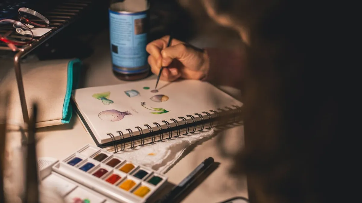 Artist painting with watercolors in a notepad at a desk. Creative process indoors.
