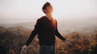 A young man standing on a misty hill during sunrise, embracing the light and nature.